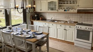 A kitchen with white cabinets, a wooden ceiling, a stove, and a dining area with a table set for four.