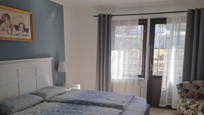 A bedroom with a bed, a chair, a radiator, and a window with curtains.