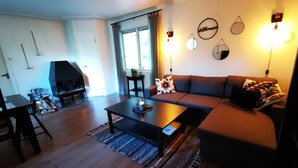 Un salon comprenant un canapé, une table basse et une cheminée. On y trouve également des appliques murales et une fenêtre avec des rideaux.