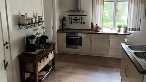 Une cuisine moderne avec des meubles en bois, un four encastré, une machine à café et une fenêtre avec des rideaux.