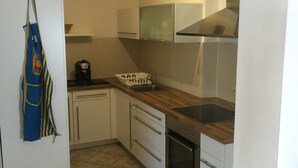 Una cuina compacta amb armaris blancs, un taulell de fusta, forn integrat i un ventilador de sostre.