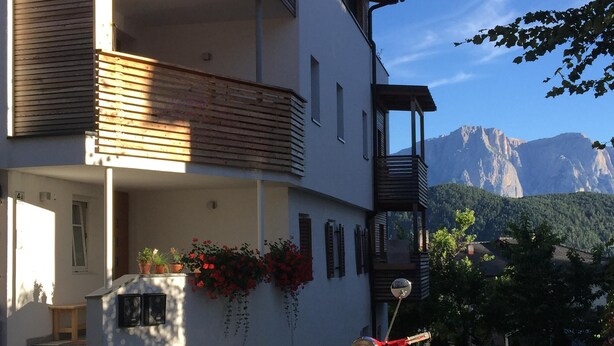 Edifici de dues plantes amb un balcó, una Vespa antiga vermella aparcada a la façana i un paisatge de muntanyes al fons.