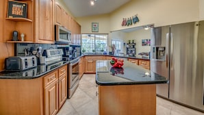 A spacious kitchen with wooden cabinets, a central island, stainless steel appliances, and a view to the outside.