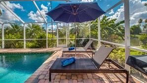 A poolside area with lounge chairs, a covered umbrella, and a view of the surrounding greenery.