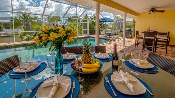 A dining table set for six with a view of a pool and palm trees.