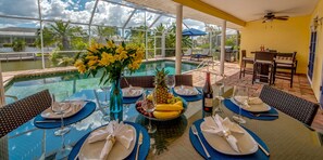 Mesa de jantar posta para seis com vista para uma piscina e palmeiras.