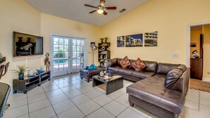 A spacious living room with a brown leather sofa, a coffee table, and a television mounted on the wall.