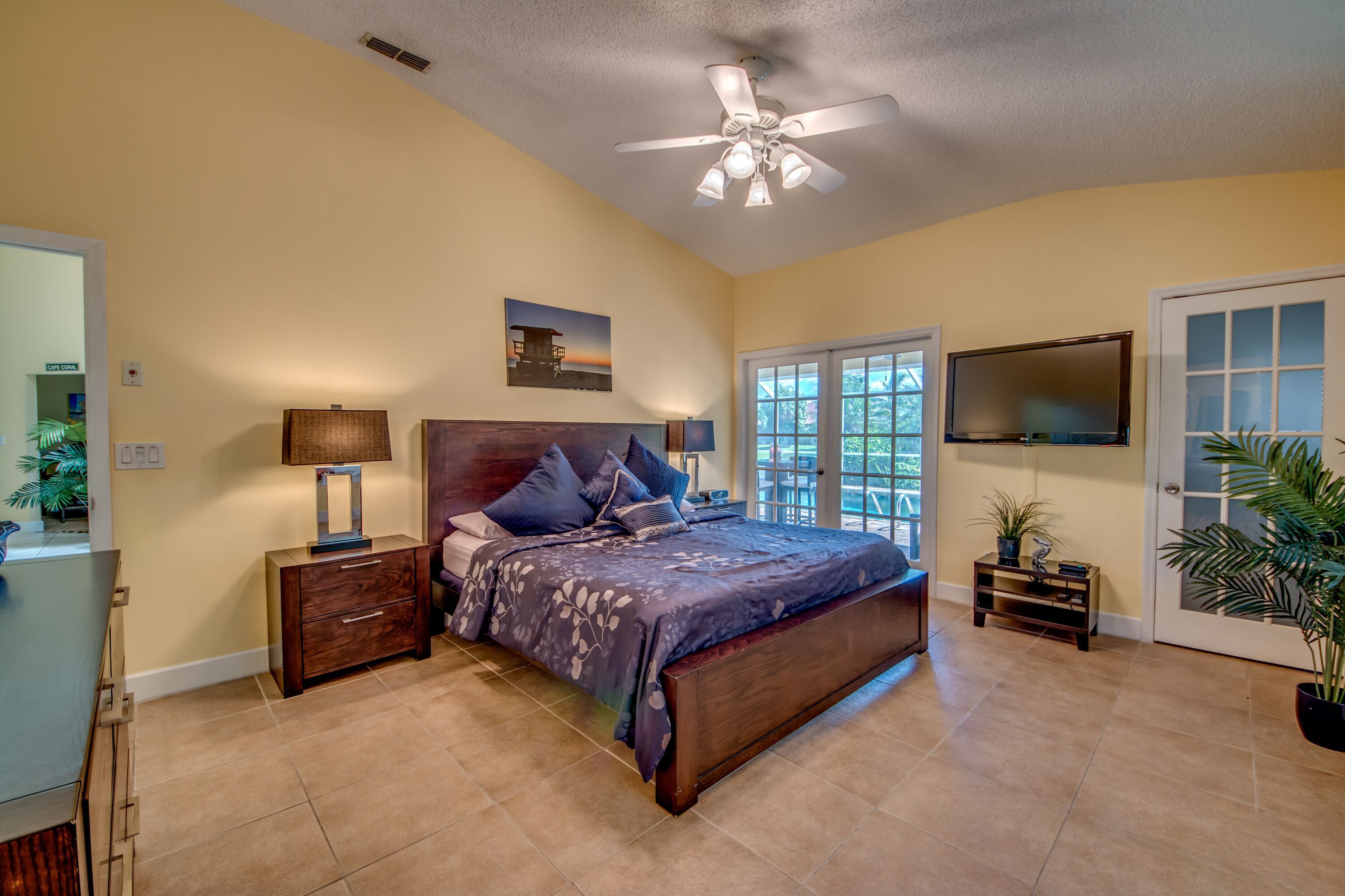 A bedroom with a bed, a ceiling fan, a TV, and a door leading outside.
