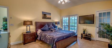 A bedroom with a bed, a ceiling fan, a TV, and a door leading outside.