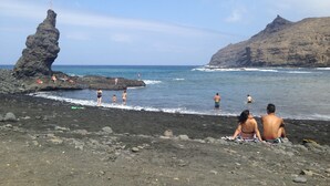 A rocky beach with a prominent rock formation and a cliff in the background.