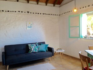 A room with a dark blue sofa, a small round table, a white rug, and a window with a green frame.