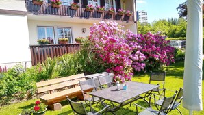 Un patio con una mesa y sillas, rodeado de abundante follaje y plantas con flores.