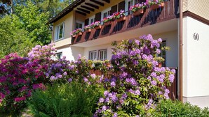 Un immeuble de deux étages doté de balcons ornés de jardinières et d’un jardin luxuriant où poussent des fleurs violettes.