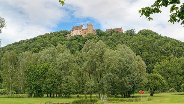 Un château perché sur une colline, avec un terrain de golf en contrebas.