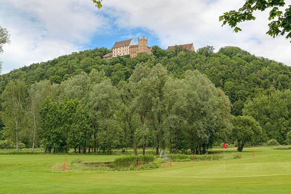Un château perché sur une colline, avec un terrain de golf en contrebas.