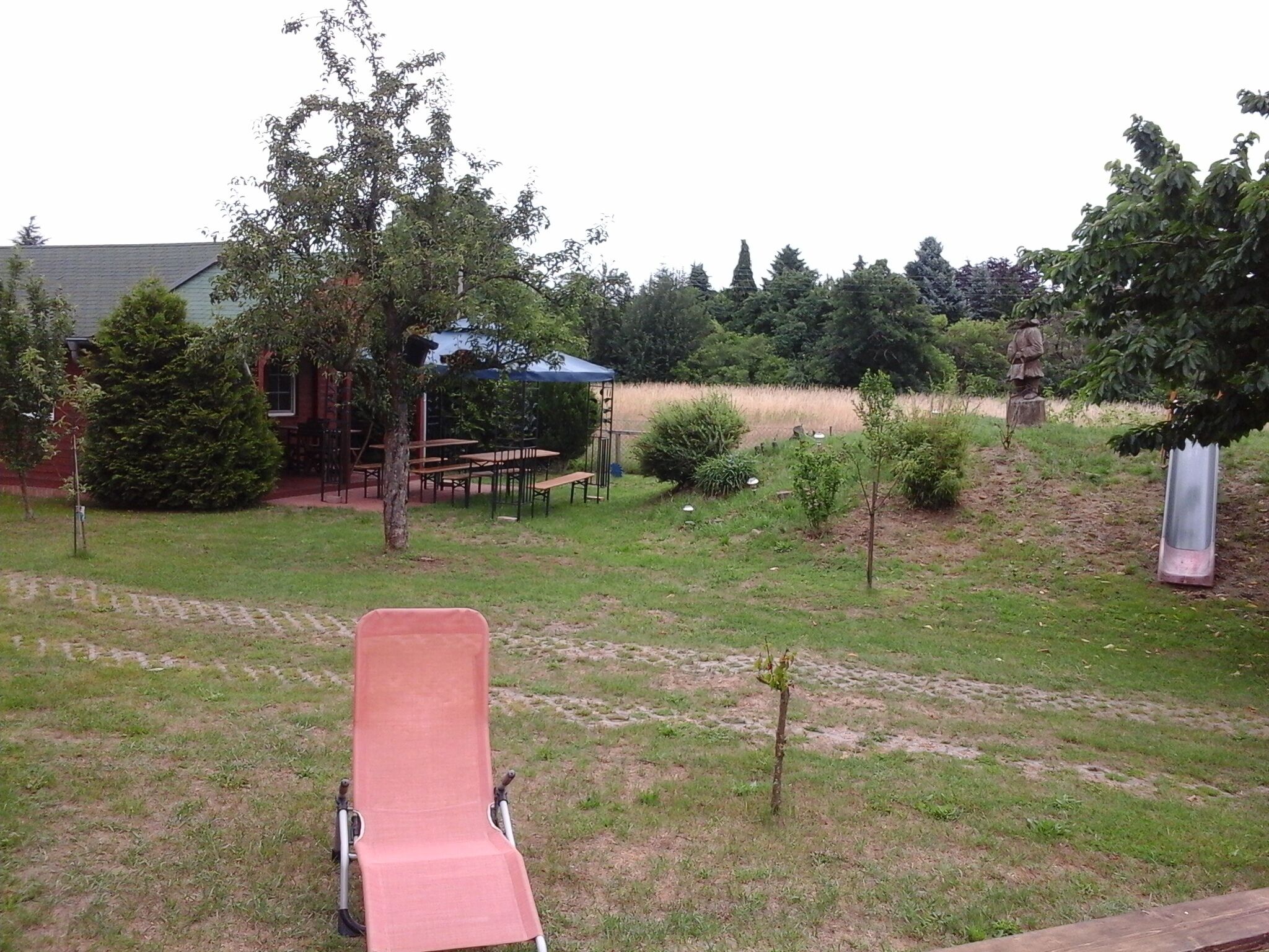 A grassy backyard with a picnic table and chairs, a small tree, and a statue.