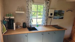 A compact kitchen with a wooden countertop, a sink, and a coffee maker. There is a window with floral curtains, a wall-mounted power outlet, and a painting of a tree. - 7 vacation homes ideal for family reunions not far from the Spreewald. (Lübbenau/Spreewald)