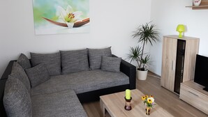 A modern living room with a grey sectional sofa, a coffee table with decorative items, a potted plant, and a wooden cabinet with a television.