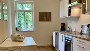 Et moderne køkken med hvide skabe, indbygget ovn og et vindue med udsigt til grønne områder.