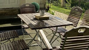 En udendørs patio med et træbord og stole, en lille dekorativ krone, og udsigt til en by i baggrunden.
