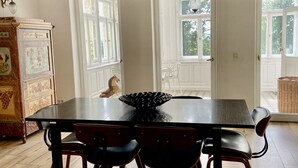 En spisestue med et stort bord, fire stole, en lysekrone og et skab med kunstværker.
