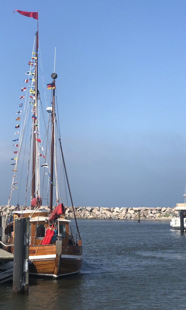 Un barco de madera amarrado en un muelle con varias banderas, una costa rocosa y agua tranquila.