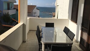 Un balcon avec une table et des chaises, offrant une vue sur la côte, avec des bâtiments et la mer.