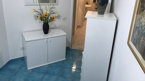 Un couloir avec une armoire blanche, un vase de fleurs et un miroir au mur.