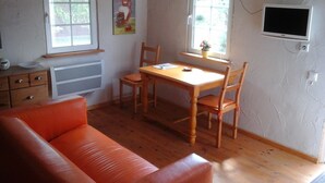 Una habitación pequeña y acogedora con una mesa y sillas de madera, un sofá y dos ventanas.
