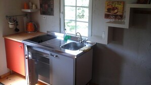Cocina compacta con un lavamanos doble, una ventana pequeña y un estante con utensilios de cocina.