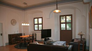 A living room with a wooden dining table, a television, a sofa, and a lamp. - Apartment in historic surroundings (Müglitztal)