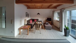 A cozy living room with a wooden ceiling, a sofa, a TV, and a potted plant. - Top apartment in small complex, 2-4 pers. 65sqm, balcony, 2 bedrooms. W-lan (Walkenried)