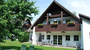 A two-story building with a sloped roof, large windows, and outdoor seating area with chairs and umbrellas. - Top apartment in small complex, 2-4 pers. 65sqm, balcony, 2 bedrooms. W-lan (Walkenried)
