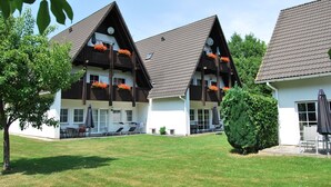 A two-story building with a sloped roof, balconies with flower boxes, and a well-maintained lawn. - Top apartment in small complex, 2-4 pers. 65sqm, balcony, 2 bedrooms. W-lan (Walkenried)