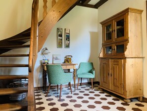 Une pièce dotée d’un escalier en bois, d’un bureau avec deux chaises, d’une armoire et d’un sol carrelé à motifs hexagonaux.
