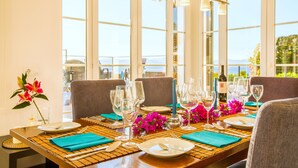 A dining table set for six with a view of the sea through large windows.