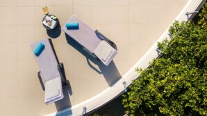 An aerial view of a poolside area with lounge chairs and a small table with a magazine and a bottle.