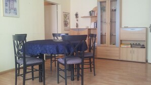 Uma área de refeições com mesa e cadeiras, um armário com livros e uma porta que dá para outro cômodo.