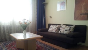 Sala de estar com sofá, mesinha com um vaso de flores, tapete estampado e abajur.