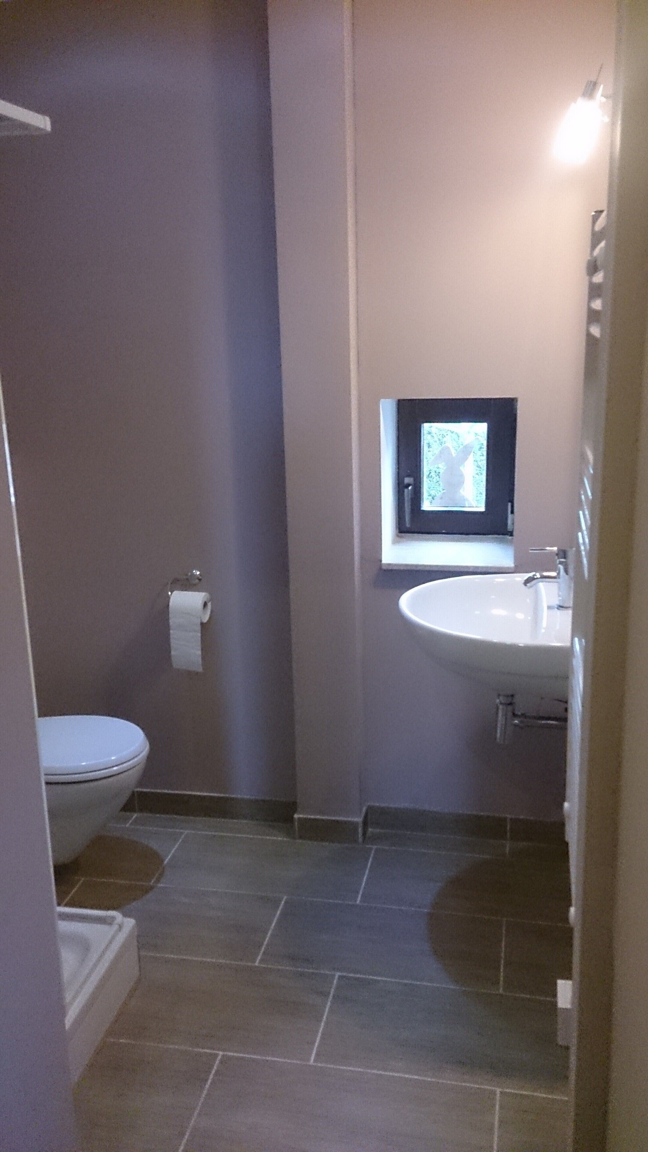 A small bathroom with a toilet, a sink, and a window above the sink.