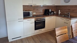 Cocina compacta con armarios blancos, microondas, cafetera, tostadora y lavabo.
