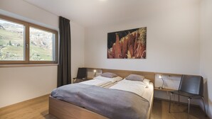 A bedroom with a wooden bed, two bedside tables, a chair, a window with curtains, and a painting on the wall. - Messnerhof winery, lovingly furnished, on the outskirts of Bolzano (Bozen)