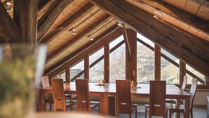 A dining area with a wooden table and chairs, large windows, and a sloped ceiling. - Messnerhof winery, lovingly furnished, on the outskirts of Bolzano (Bozen)