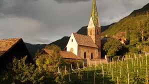 A church with a tall spire, surrounded by vineyards and houses on a hillside. - Messnerhof winery, lovingly furnished, on the outskirts of Bolzano (Bozen)