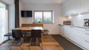 A modern kitchen with a wooden table, two chairs, a window with curtains, a flat-screen TV, and a coffee machine. - Messnerhof winery, lovingly furnished, on the outskirts of Bolzano (Bozen)