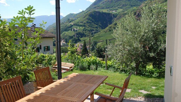 A wooden table and chairs under a covered patio with a view of a mountainous landscape. - Messnerhof winery, lovingly furnished, on the outskirts of Bolzano (Bozen)