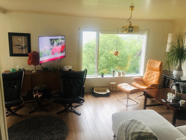 A living room with a TV, two chairs, a sofa, a coffee table, and a window with a view of greenery. - Stunning views to the mountains and sea, sleeps 6people. (Gurskøy)