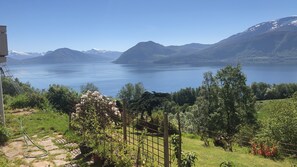 A view of a lake with mountains in the background, surrounded by greenery and a metal fence. - Stunning views to the mountains and sea, sleeps 6people. (Gurskøy)