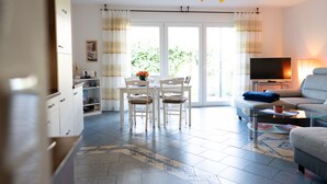 Ein modernes Wohnzimmer mit Essbereich, einer Couch, einem Fernseher und einer Küchenzeile.