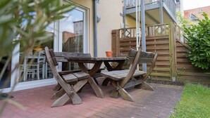 Eine Terrasse mit Holztisch und -stühlen, einem Blumentopf und Blick auf ein Gebäude mit Balkon.